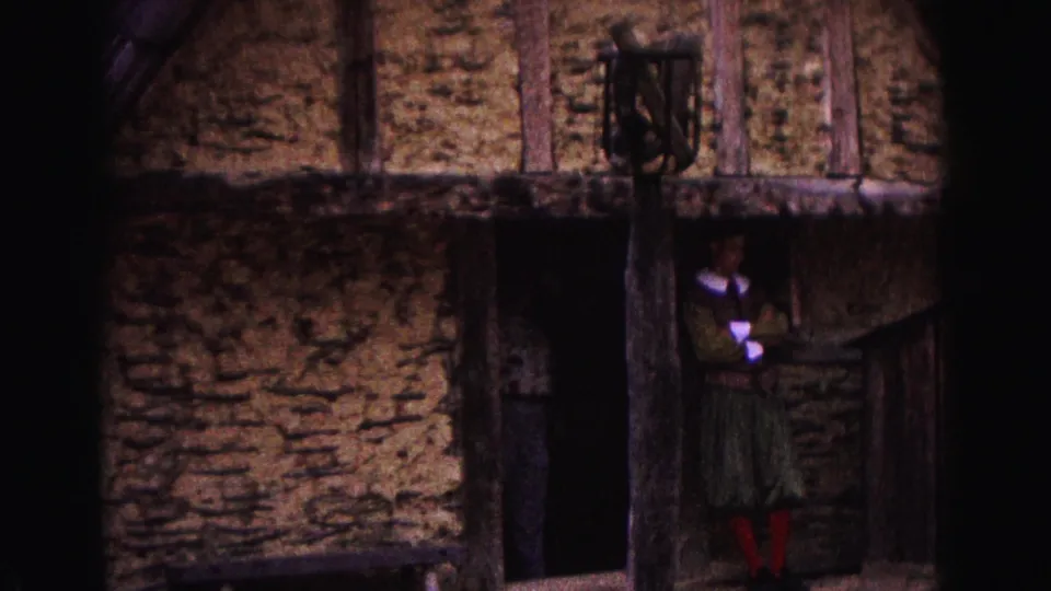 1964 Williamsburg footage showing a rustic thatched structure with rough walls, timber supports, and a person near the doorway.