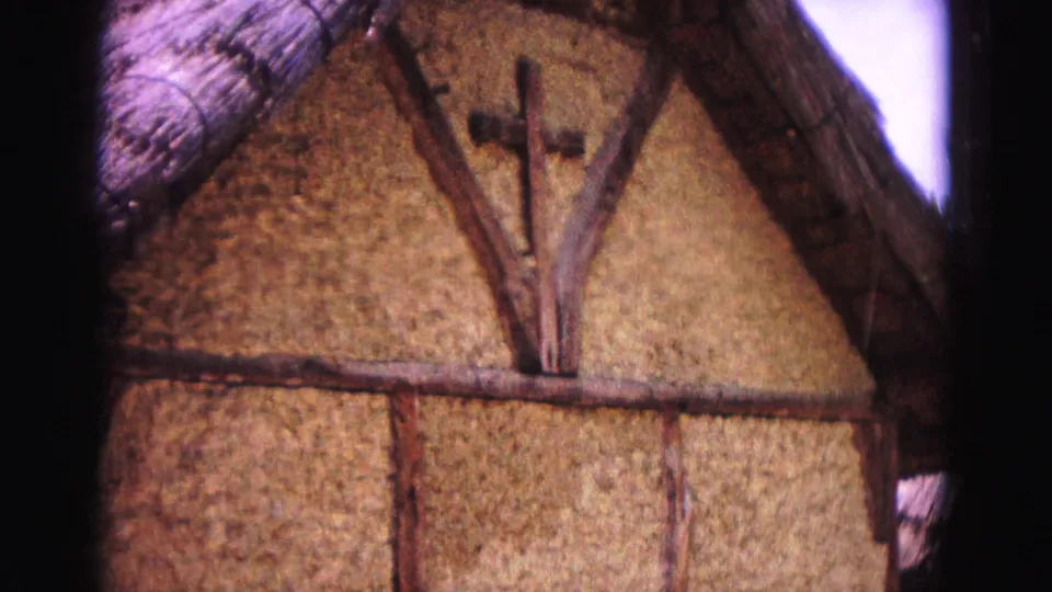 1964 Williamsburg frame showing a thatched-roof building wall with a wooden cross and exposed timber framing.