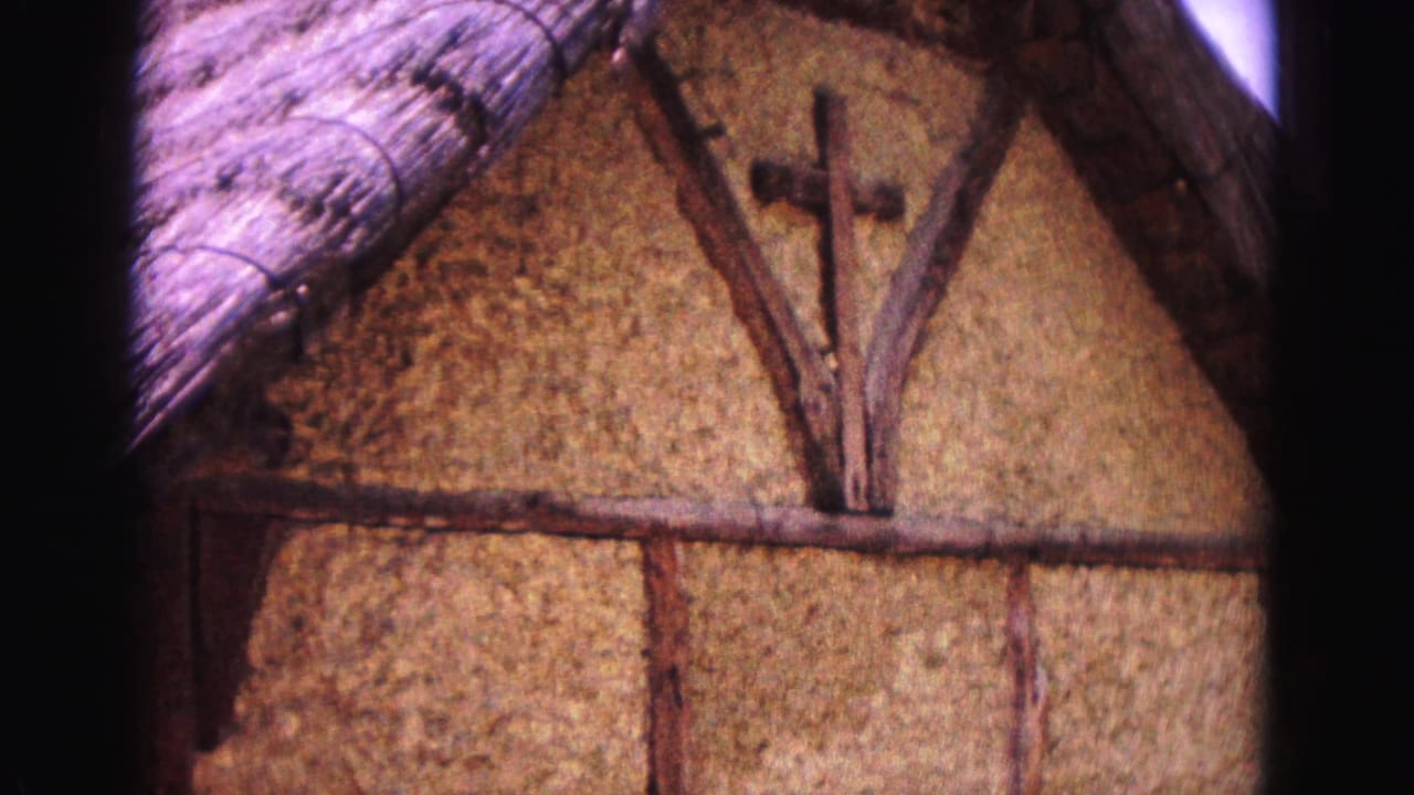 Close view of a thatched gable with exposed beams and a wooden cross.