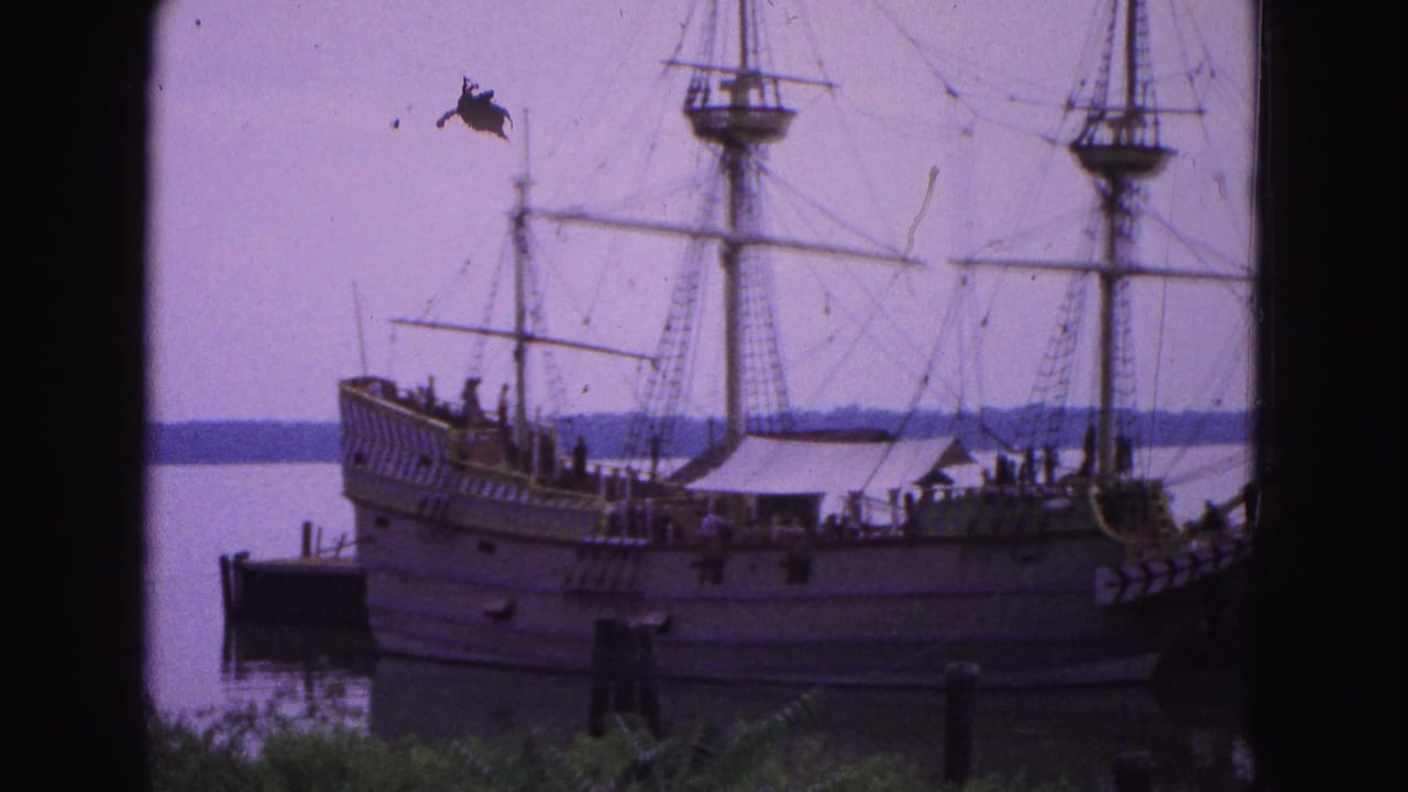 Large rigged wooden sailing vessel docked by calm water with masts and rigging visible.