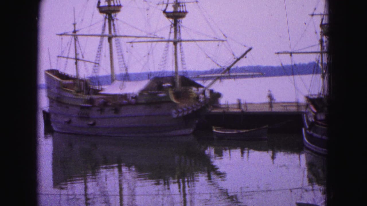 Tall ship moored beside a pier with reflections in calm harbor water.