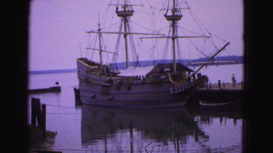 The Susan Constant replica appears docked in Williamsburg, Virginia, with rigging visible above a quiet pier and reflected harbor water.