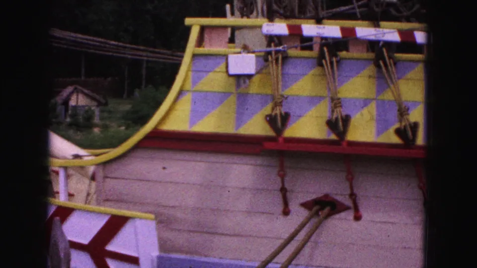 1964 Williamsburg frame of a replica ship stern with yellow and blue geometric paint, hanging anchors, ropes and small cannons.