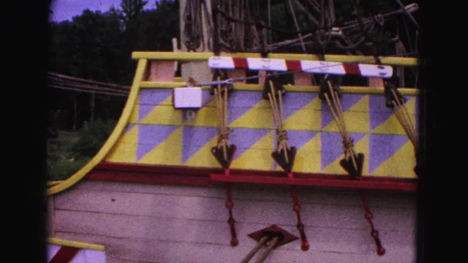 1964 Williamsburg home-movie frame showing the painted stern area of a historic-style ship with yellow and lavender diamonds and red trim.