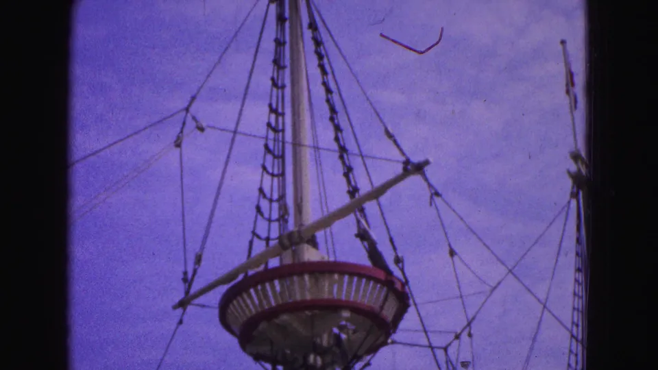 1964 Williamsburg frame looking upward at the mast, crow's nest, and rigging of a historic-style ship display.