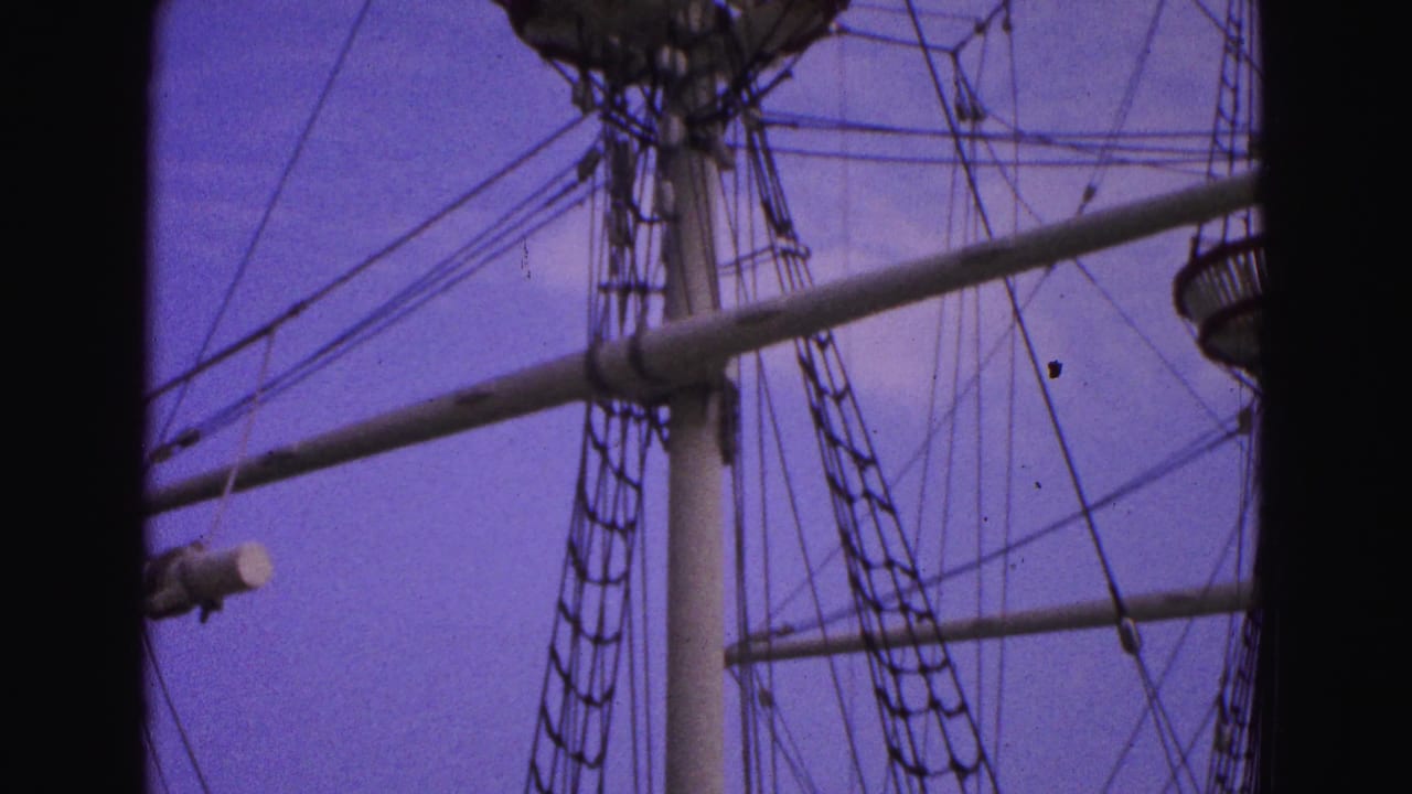 Tall ship masts and rigging seen against a purple-blue sky with dark film borders.