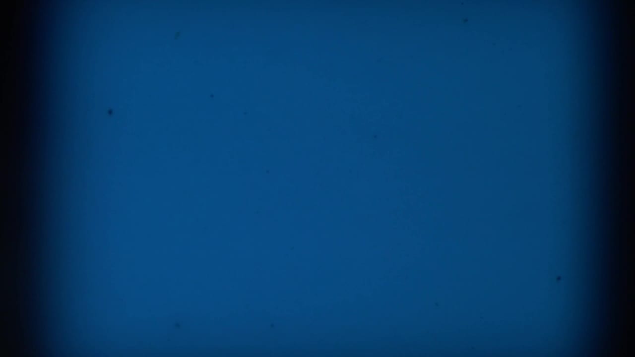 Blue leader-like 8mm frame from the 1965 Clarkson, Nebraska clip, with dark borders, grain, and small specks.
