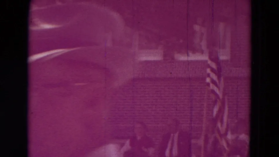 Magenta 1965 Clarkson, Nebraska frame showing a faint person near an American flag with a house-like background.
