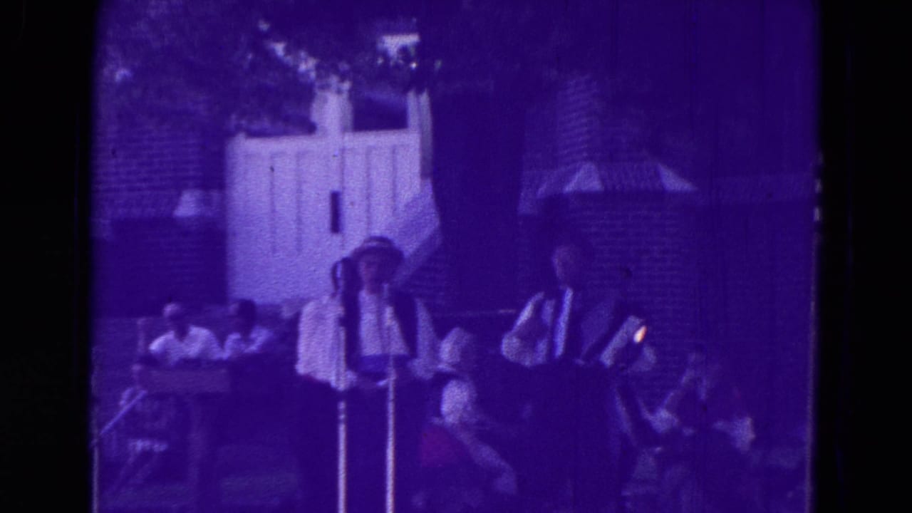 1965 Clarkson, Nebraska home-movie frame showing musicians or singers at microphones during an outdoor community performance.