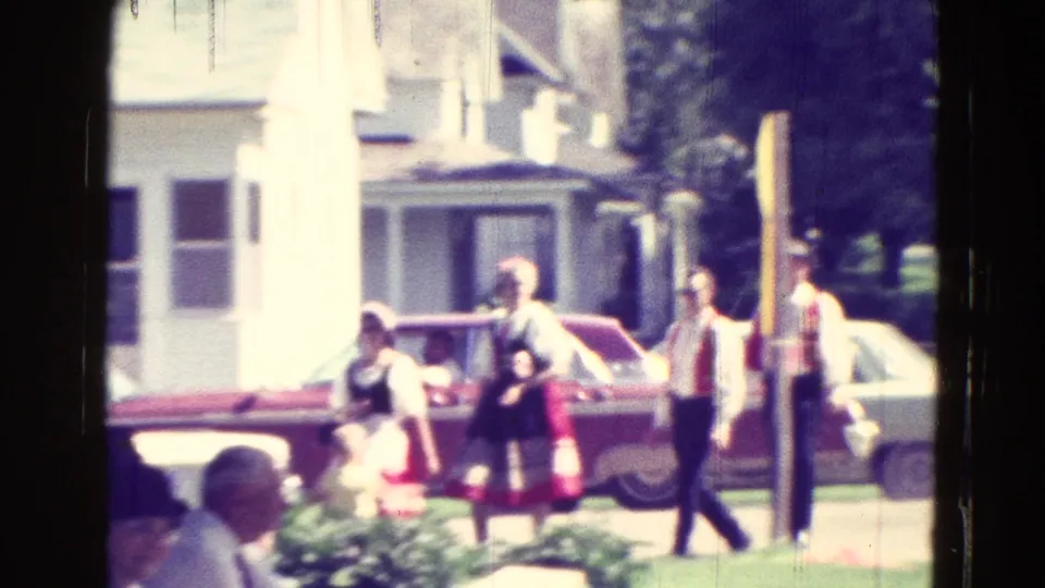 1965 Clarkson, Nebraska home-movie frame showing people near a red car, including women in traditional-looking dress by a white house.