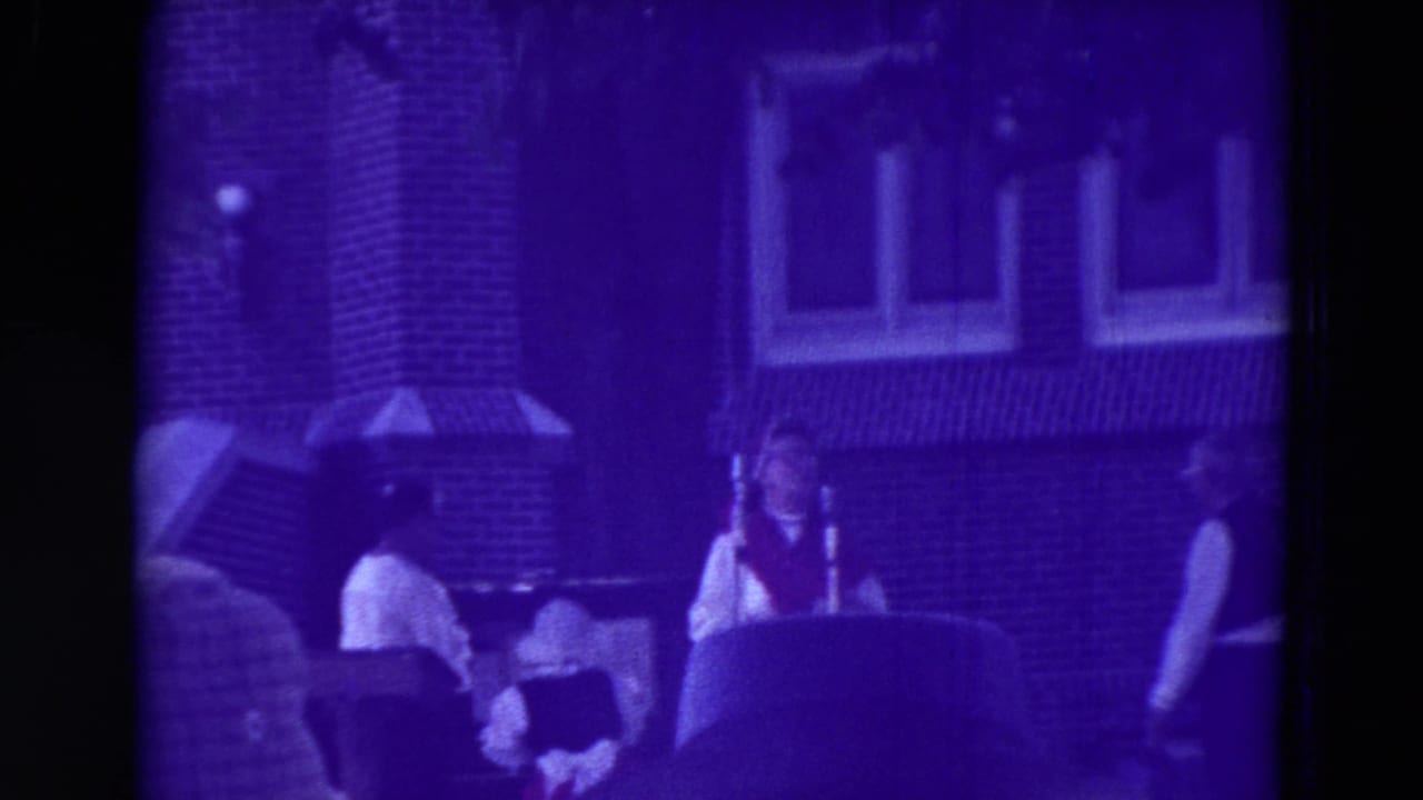 1965 Clarkson, Nebraska carnival footage shows workers in white shirts and vests beside seated visitors near a brick building and canopy.