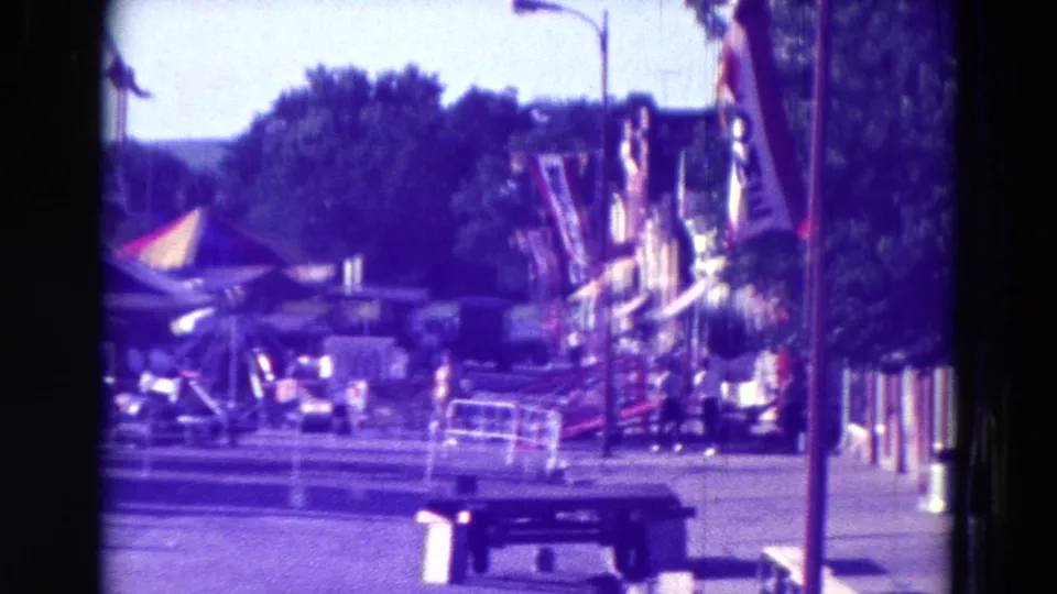 1965 Clarkson, Nebraska fairground view with tents, benches, poles, trees, and parts of carnival rides visible in a grainy 8mm frame.
