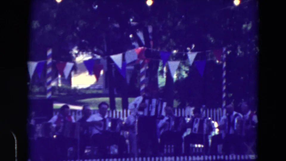 1965 Clarkson, Nebraska home-movie frame showing accordion musicians and spectators at an outdoor community festival.