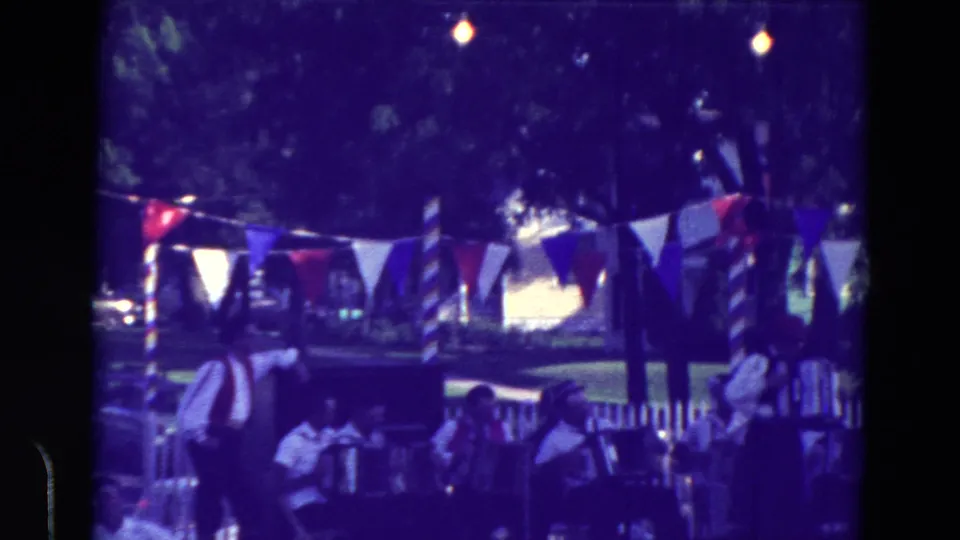 1965 home-movie frame from Clarkson, Nebraska showing accordion performers and audience members under festival bunting.