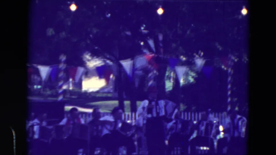 Purple-shifted 8mm frame of a Clarkson, Nebraska community festival with accordion players and spectators outdoors.