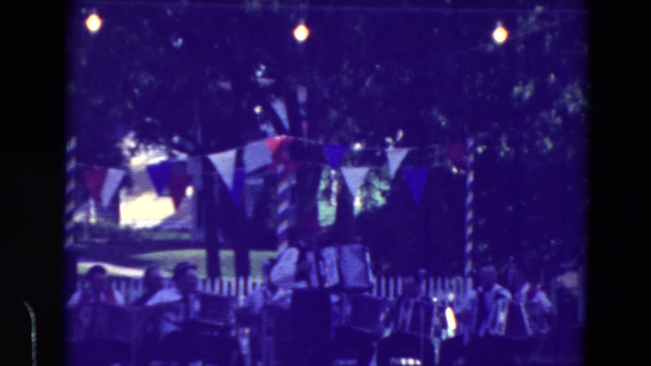 Accordion band playing outdoors under bunting and string lights at dusk.