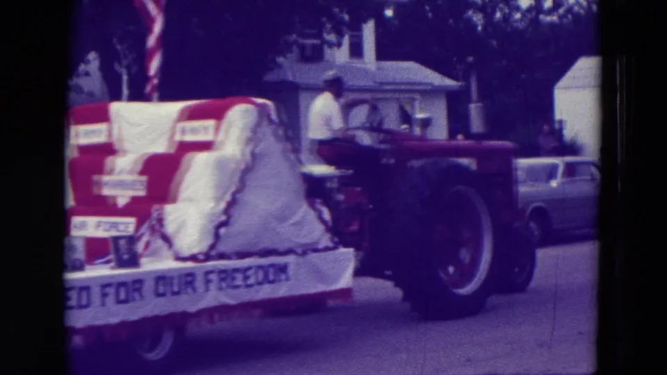 A red tractor pulls the veterans tribute float, with red-white-blue decoration and a banner partly reading about freedom.