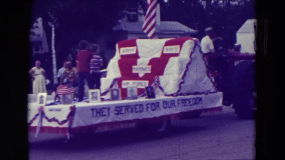 The Clarkson parade float shows patriotic bunting, an American flag, riders, and a banner reading THEY SERVED FOR OUR FREEDOM.