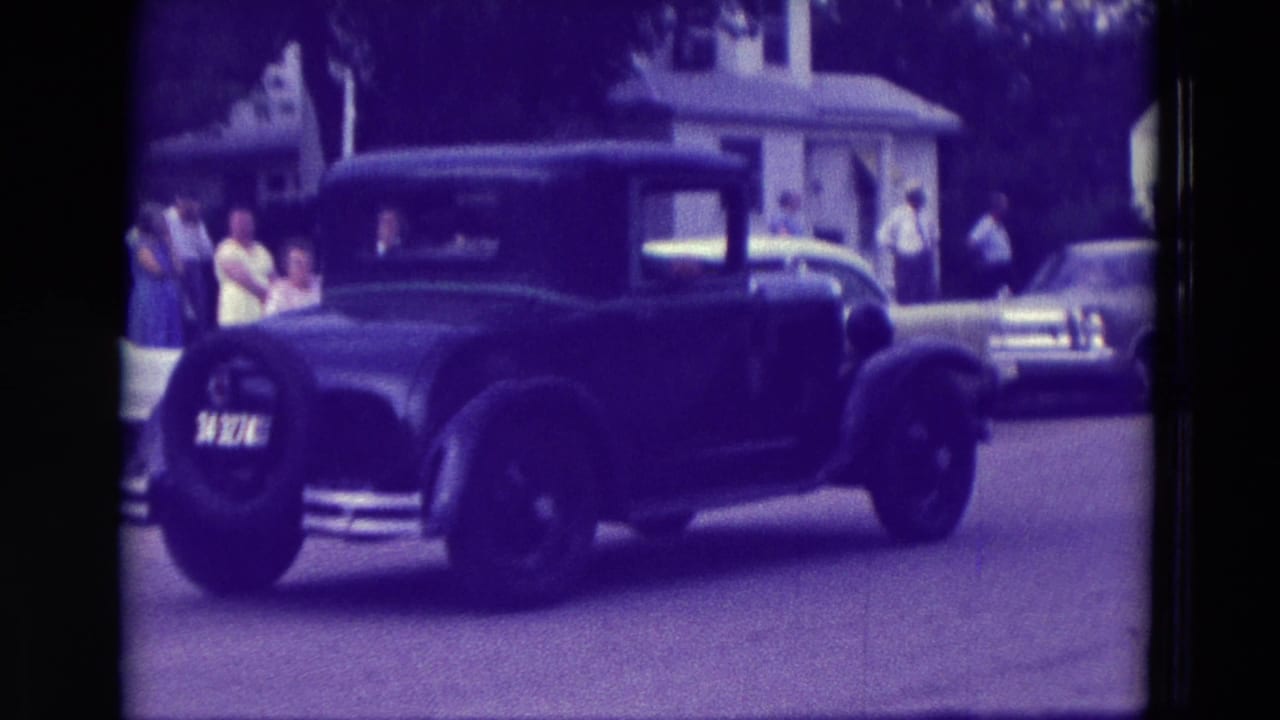 Black vintage sedan passing spectators on a residential street.