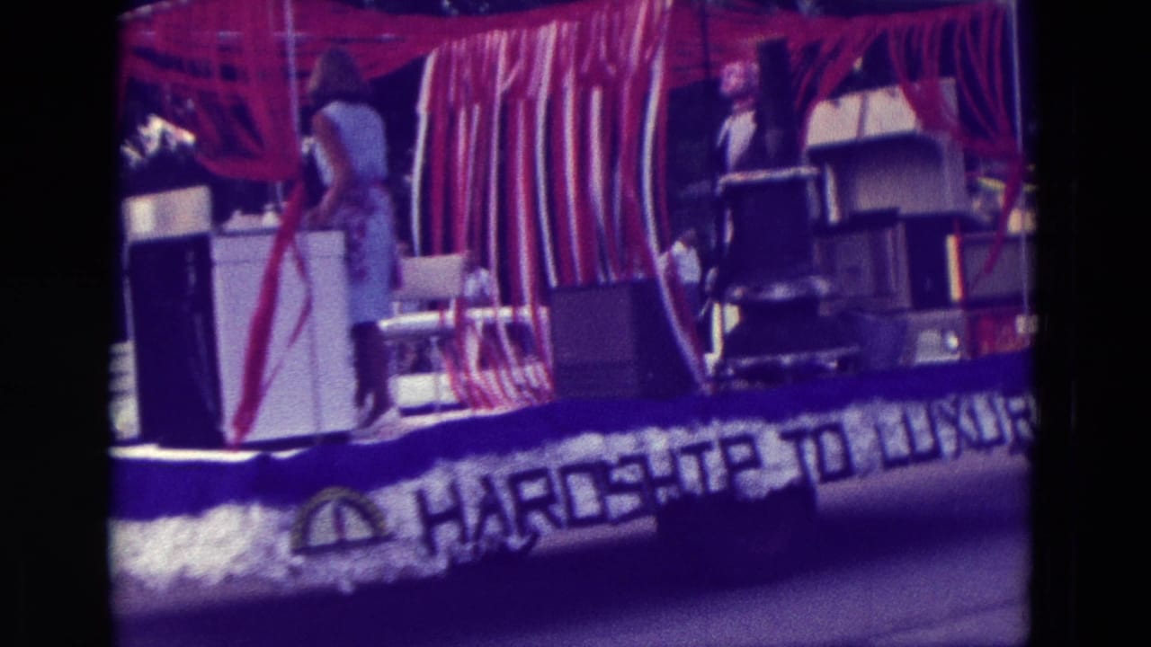 1965 Clarkson, Nebraska float decorated with red and white streamers, appliances, a woman, and Hardship to Luxury lettering.