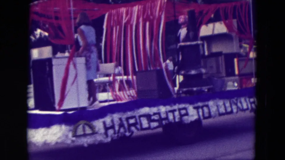 1965 Clarkson, Nebraska float decorated with red and white streamers, appliances, a woman, and Hardship to Luxury lettering.