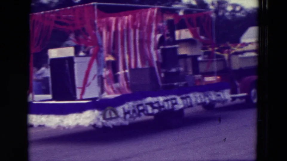 1965 Clarkson, Nebraska parade float seen broadside with striped curtain, appliance display, and Hardship to Luxury banner.