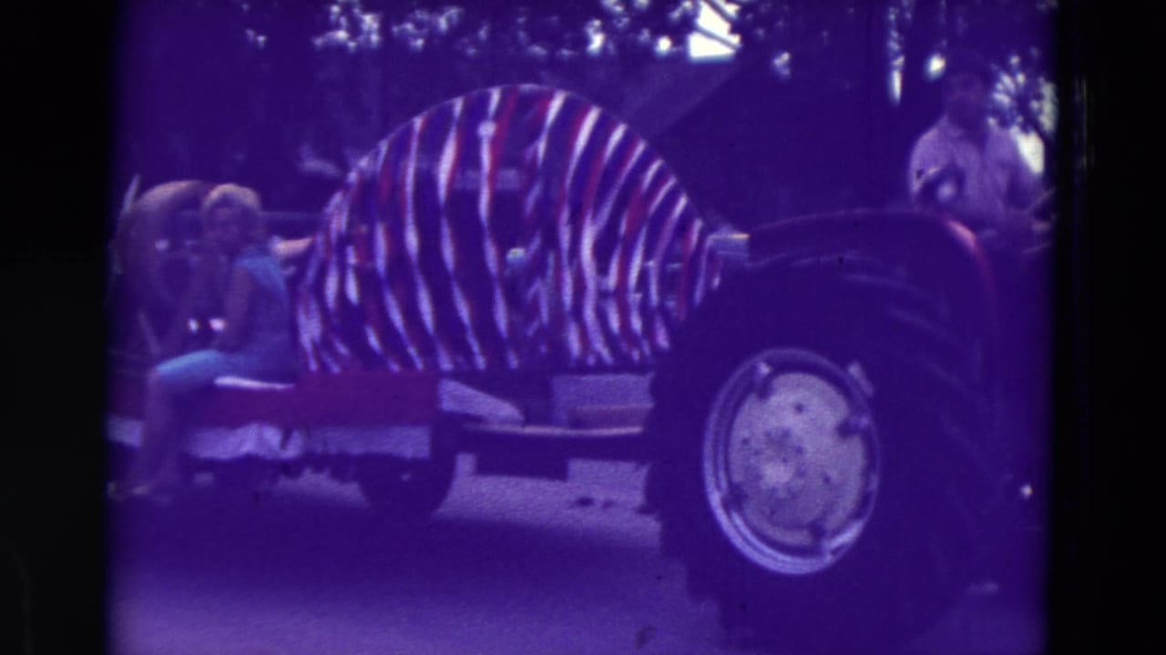 1965 Clarkson, Nebraska home-movie frame showing a tractor-pulled parade float with striped decoration and spectators nearby.