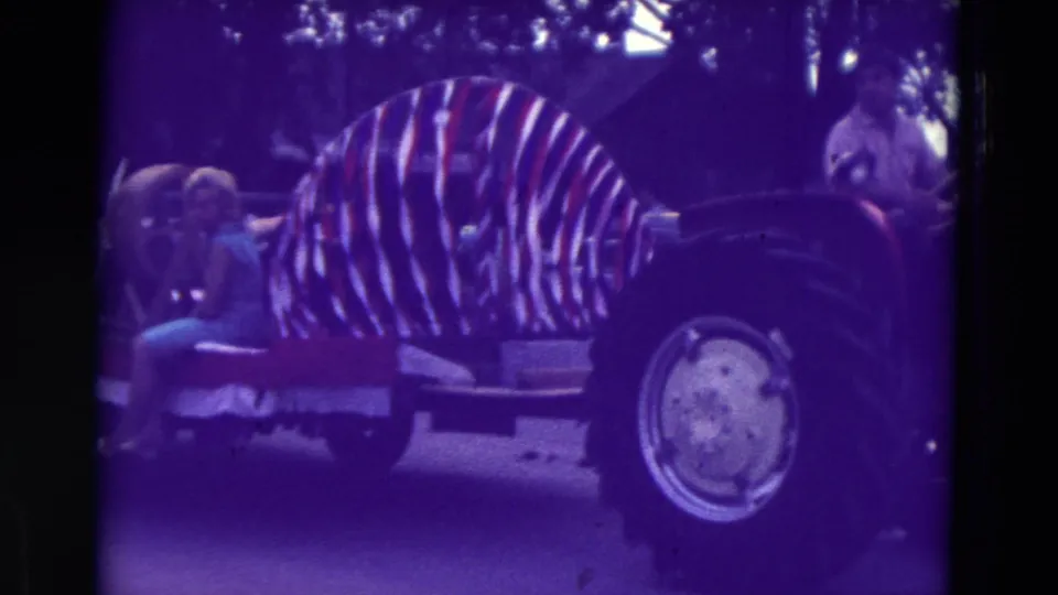 1965 Clarkson, Nebraska home-movie frame showing a tractor-pulled parade float with striped decoration and spectators nearby.