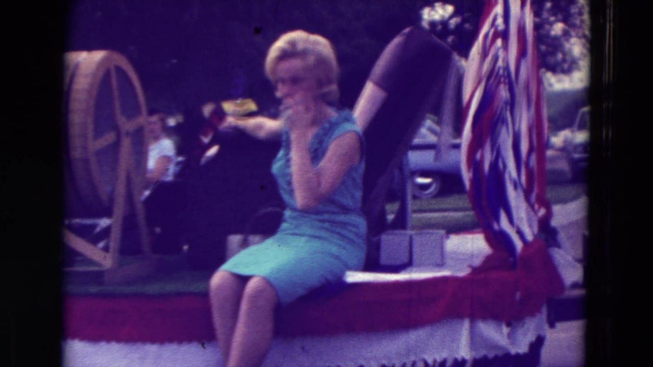 A blonde woman in a sleeveless blue dress rides on a patriotic parade float in Clarkson, Nebraska, in 1965.