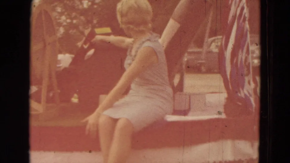 A warm, faded 8mm frame shows the seated woman on the Clarkson parade float with red, white, and blue decoration nearby.