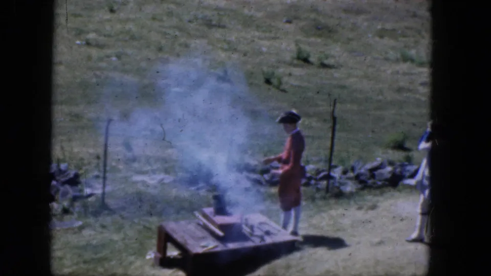 A 1965 Concord reenactment scene shows a red-coated figure near a smoking wooden platform in an open field.