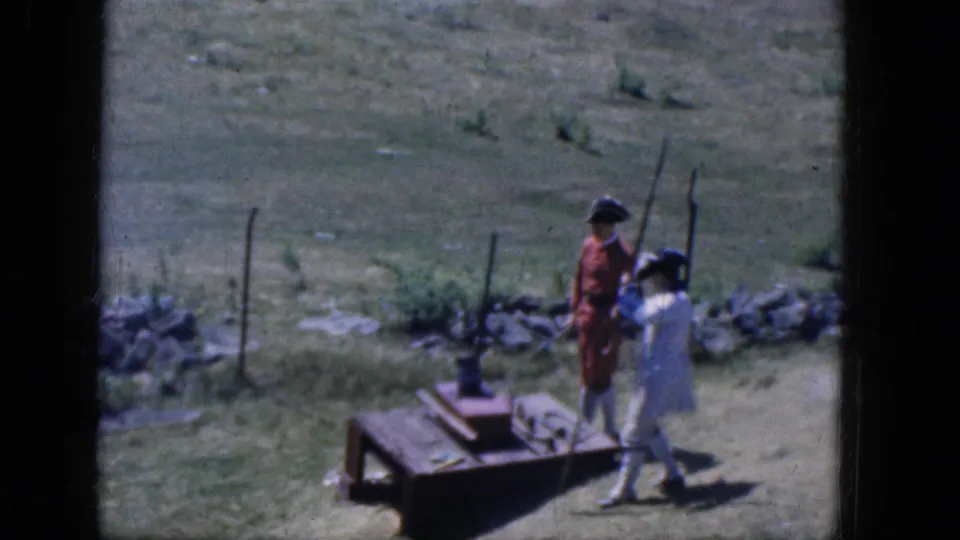 In the final frame, the reenactors in red and white period clothing move around the wooden weapon-test platform in Concord.