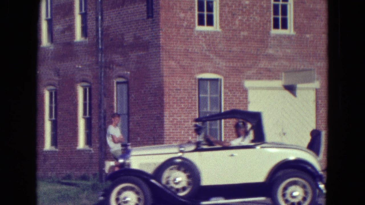 Cream-colored convertible with black soft top and whitewall tires beside a brick building in the supplied 1965 Diller, Nebraska setting.
