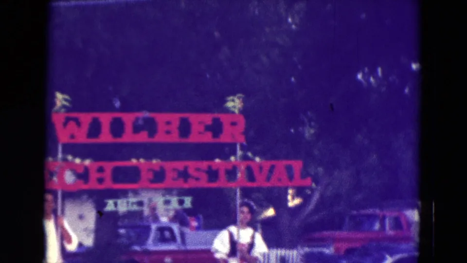 Diller, Nebraska festival frame with a red banner that appears to read Wilber and festival, with people and parked cars below.