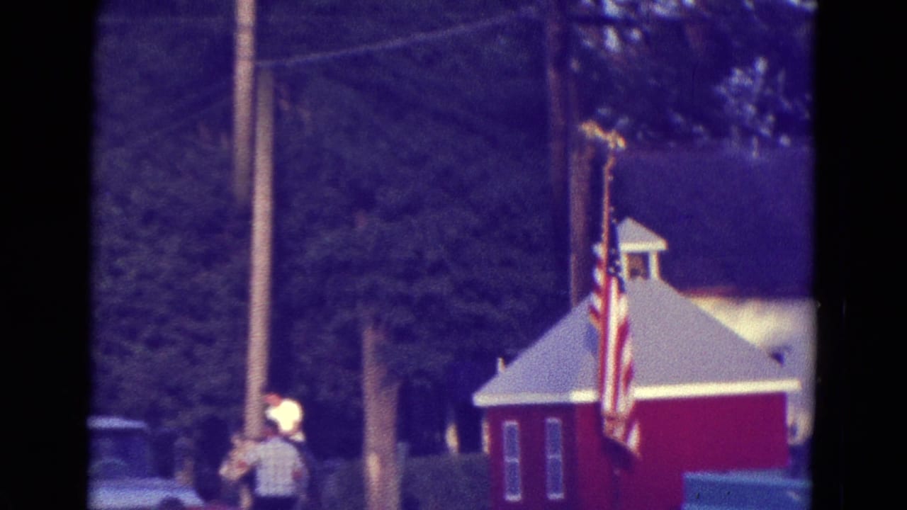 Person near a pole and American flag beside a red building and trees.