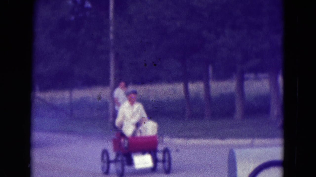 Red go-kart moving along a street with two white-clad figures visible.