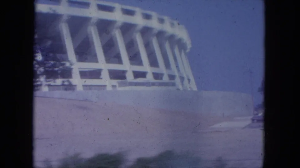 1965 Louisville frame with the stadium's curved white exterior, concrete wall, roadway edge, and open sky.