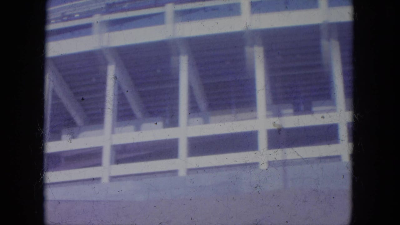 1965 Louisville home-movie frame showing a partial white stadium structure with empty bleachers and heavy 8mm gate edges.