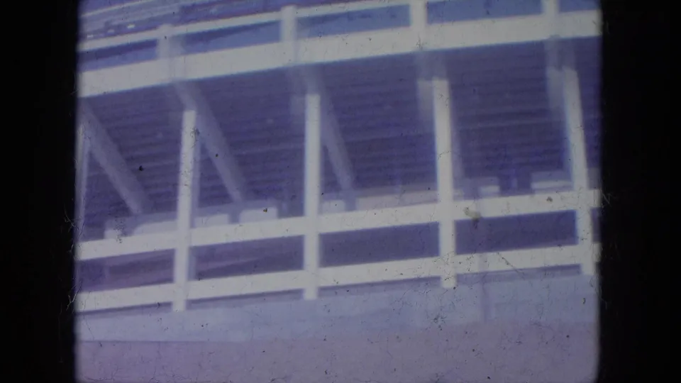 1965 Louisville home-movie frame showing a partial white stadium structure with empty bleachers and heavy 8mm gate edges.