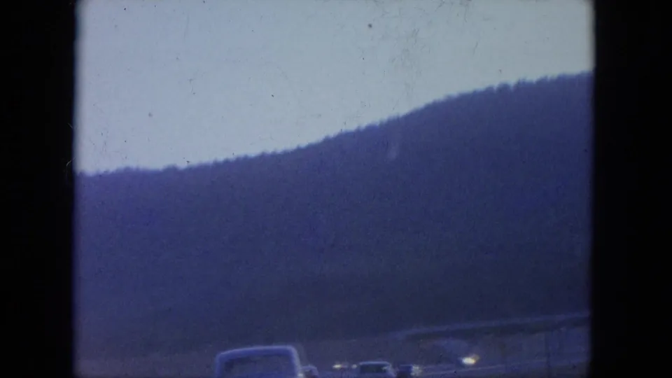 A wooded Kentucky hillside appears beyond a roadway, with soft vehicle shapes at the lower edge of the 8mm frame.