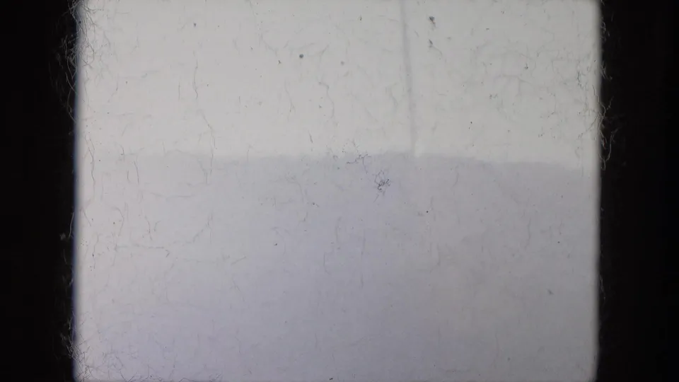 Overexposed 8mm frame with a faint hillside silhouette, pale sky and prominent dust and handling marks.