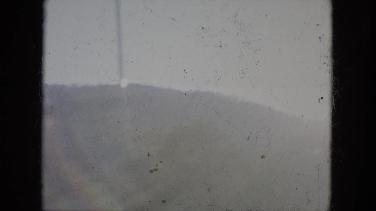 Soft distant hills seen beyond a bridge railing through an 8mm film frame.
