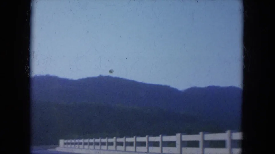 1965 Louisville-area road view from a moving vehicle, with a white bridge railing against distant hills.
