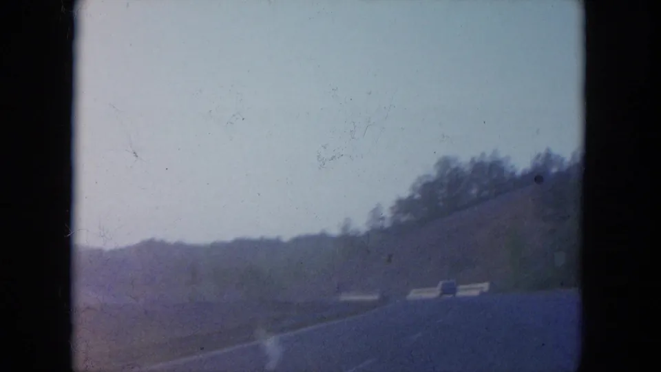 1965 Louisville-area driving view showing an open road, low hills, bare trees, and a small vehicle ahead.