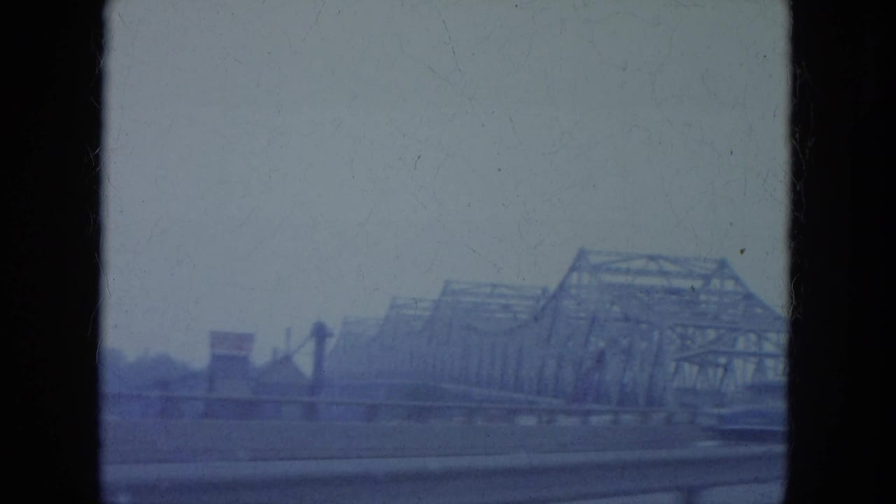 Soft blue-tinted view of steel truss bridge structures beyond a roadway.