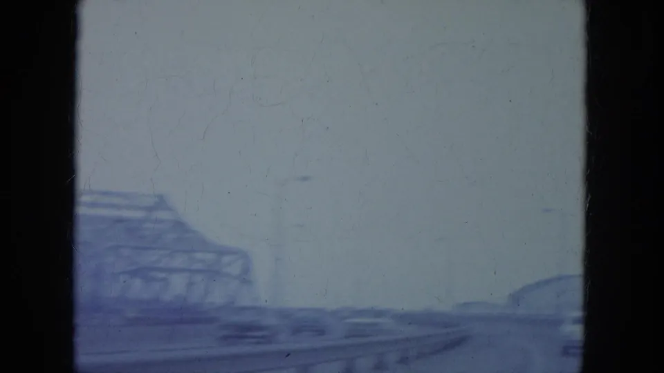 Blue-tinted 8mm frame from a moving vehicle, showing bridge framework and traffic on a Louisville roadway.