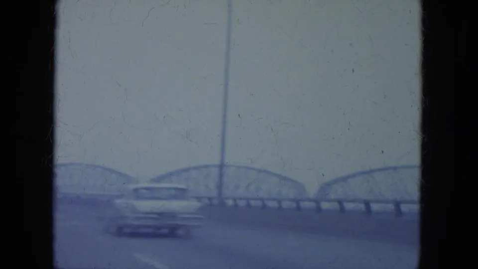 1965 Louisville roadway frame with arched bridge spans in the distance, tall light poles, and a car passing in the foreground.