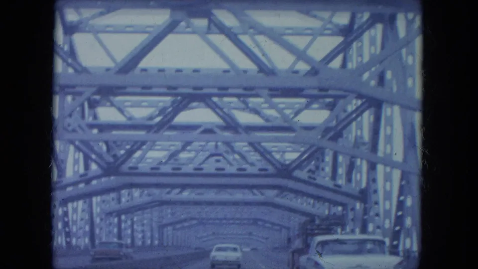 Blue-tinted 8mm frame of a Louisville steel truss bridge crossing, showing roadway lanes and mid-century cars.