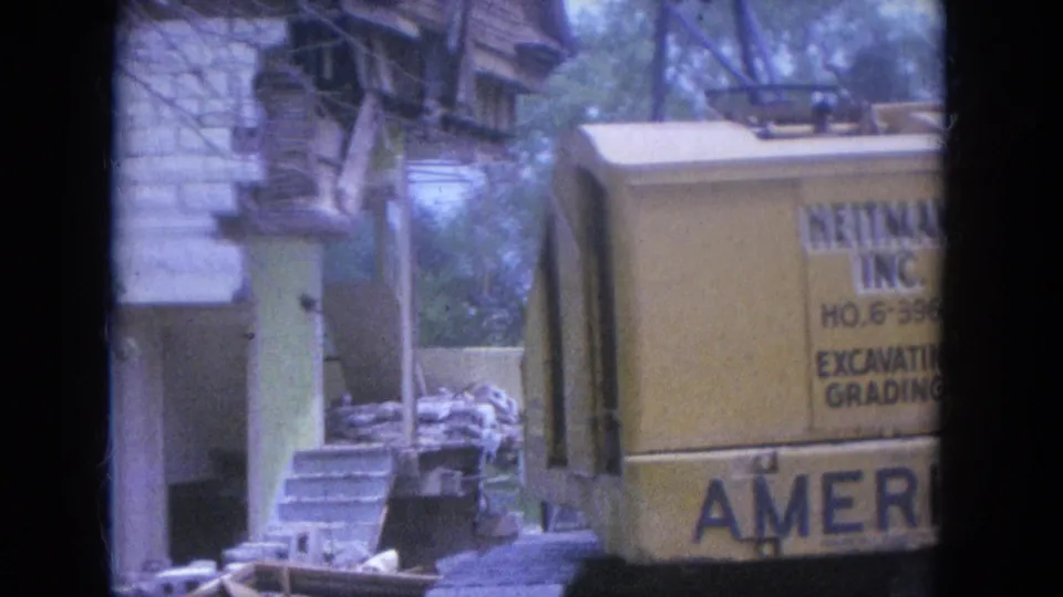 1965 Louisville frame showing a yellow construction vehicle with partial Heitman Inc. lettering near a stone house.