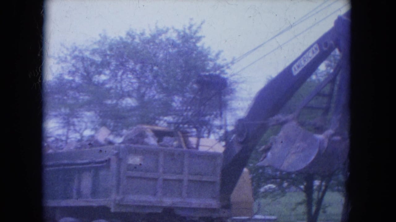 The excavator arm extends over a dump truck during debris loading in the Louisville construction scene, seen through faded 8mm color.